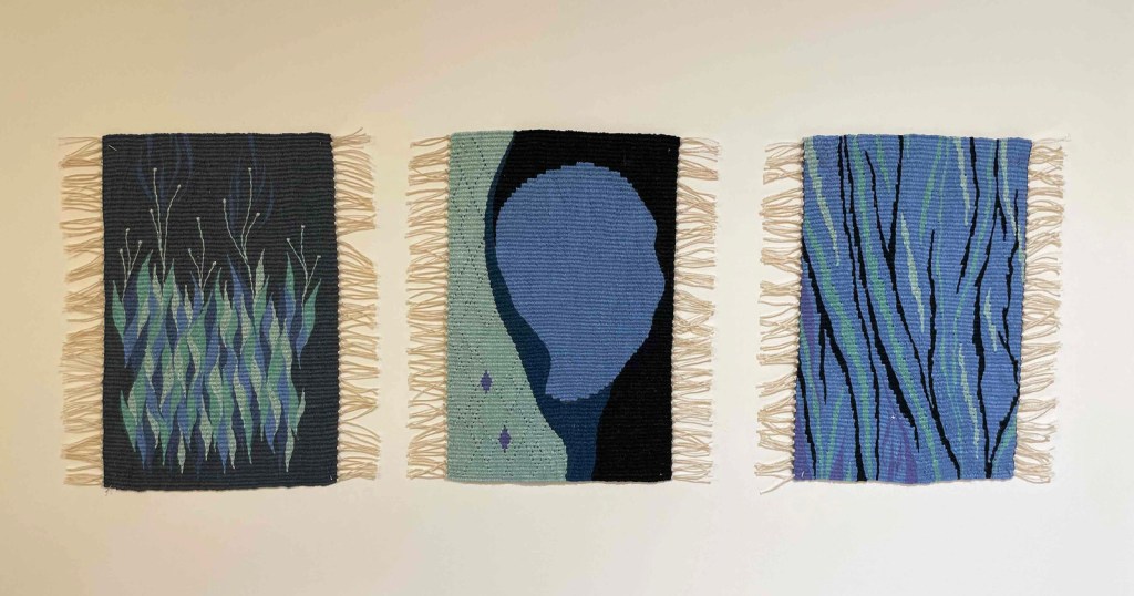 Photo of three small tapestries mounted in shades of blue, aqua, and black