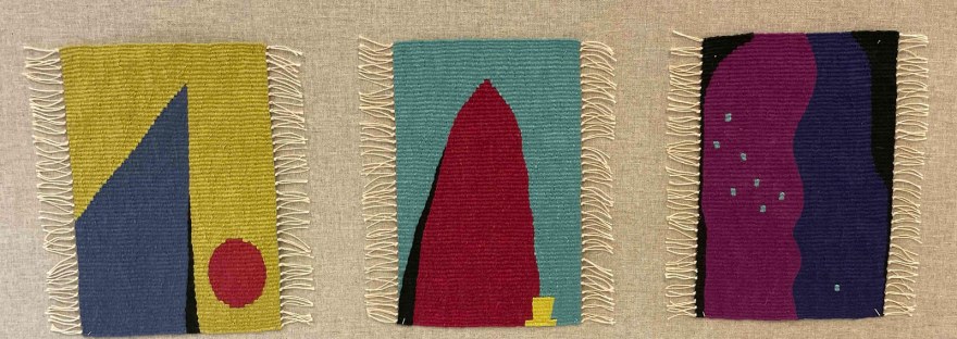 Photo of three small mounted tapestries in shades of blue, red, green, pink, purple, and black
