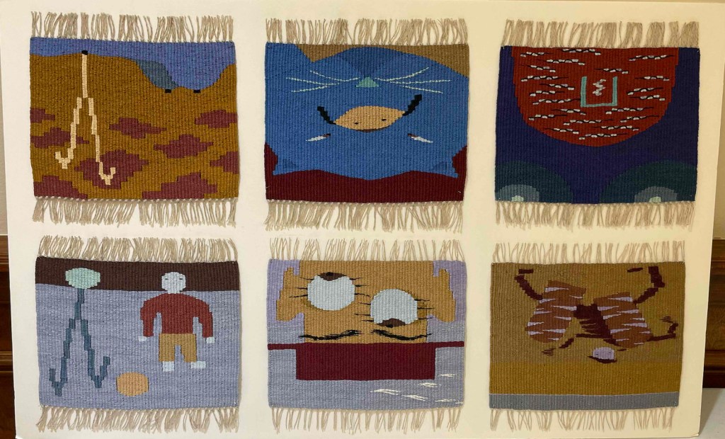 Photo of six small mounted tapestries in shades of blue, red, and tan