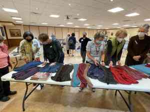 Photo of people standing by tables with various garments on them.