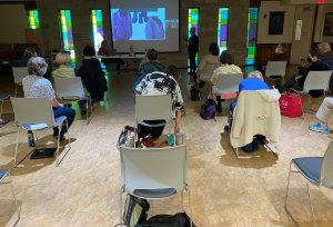 Photo of people in chairs watching presentation, taken from the back of the room looking forward toward the speaker, Dianne Totten.