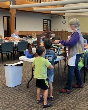 Photo of a woman helping two young boys weave on a table loom.