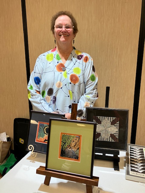 Woman standing behind several framed, beaded pictures.