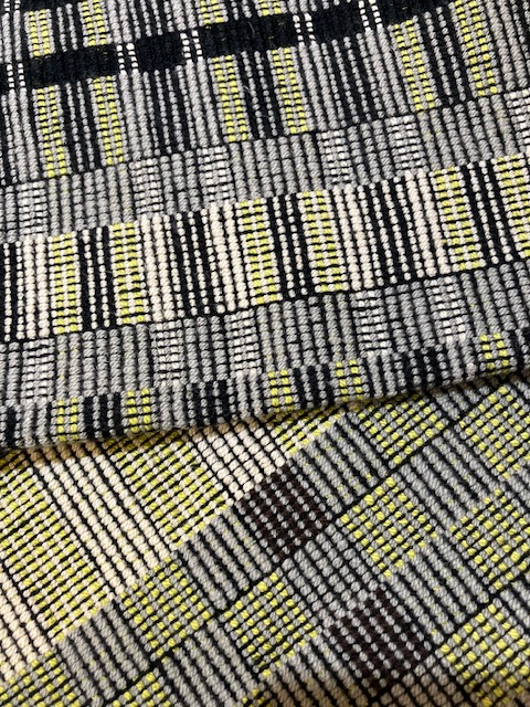 Close-up of two multi-patterned towels woven in shades of green, cream, gray, and black, incorporating stripes, checks, and color-and-weave effects.