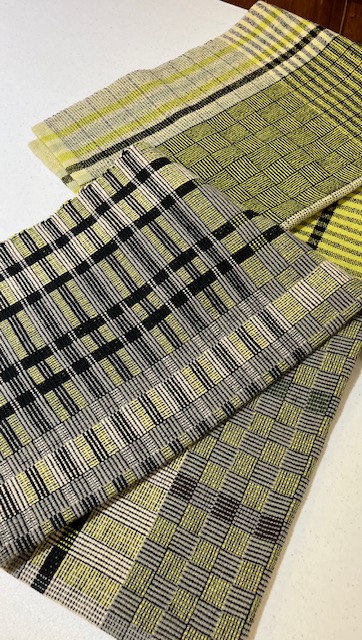 Two multi-patterned towels woven in woven in shades of green, cream, gray, and black, incorporating stripes, checks, and color-and-weave effects.