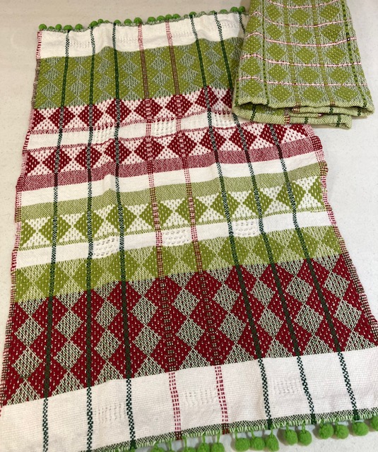 Two towels woven in shades of green cream, and red, icorporating texture, diamond patterns, lace texture accents, and stripes.