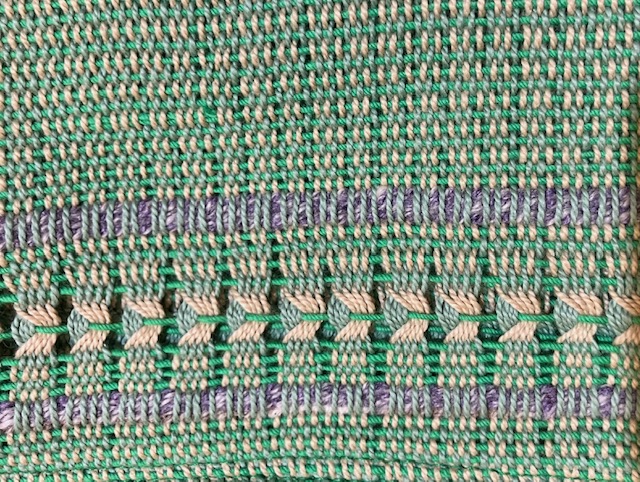Close-up of towel woven in shades of green, blue, and gray, with texture and Leno lace at the edge.