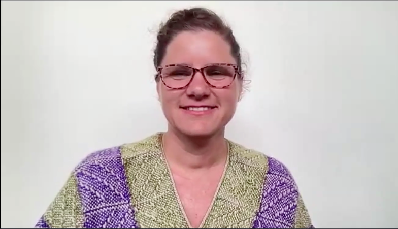 A woman wearing glasses and a shirt made with pieced pin loom-woven squares in shades of purple and white and green and white