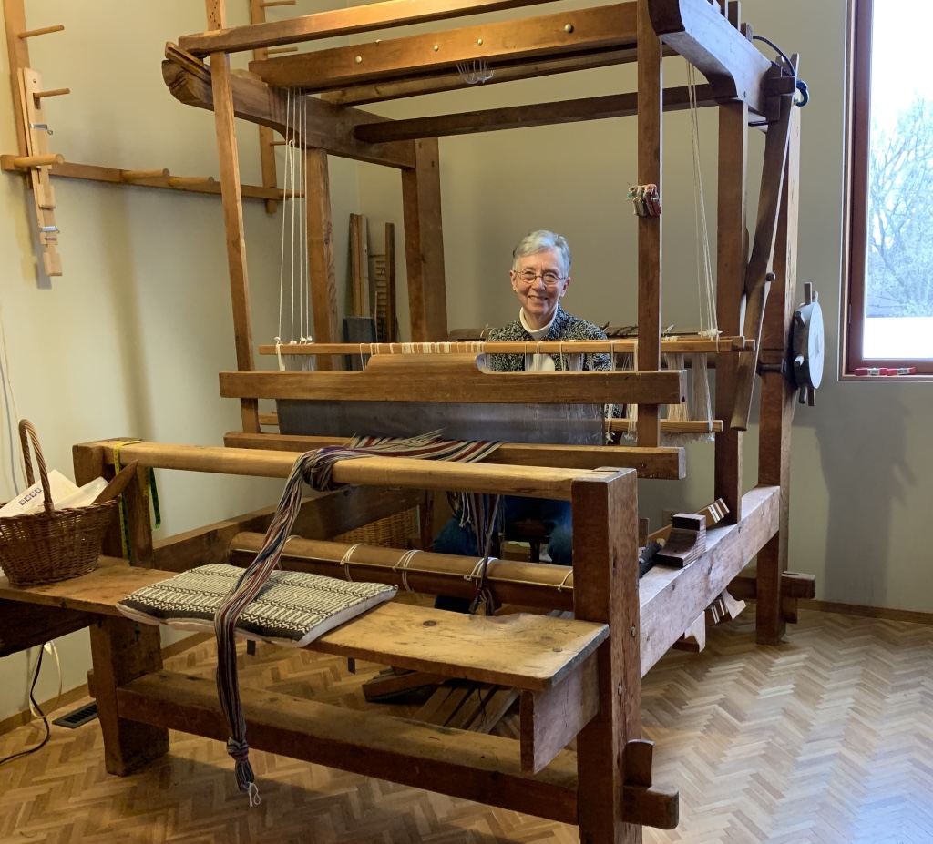 Woman sitting inside a large barn-style loom to thread it