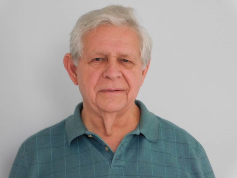 Portrait photo of man with white hair wearing a teal shirt