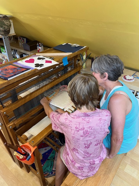 Jodi and grandson Chase sitting at a floor loom and weaving together.