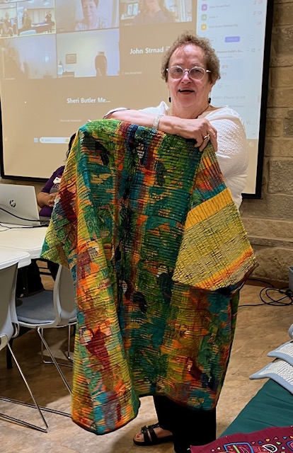 Woman holding a vibrant kimono-style coat woven in shades of yellow, green, black, red, aqua, and orange.