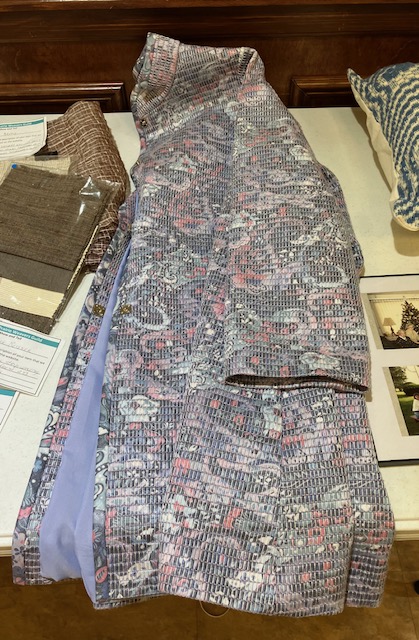 Raincoat laid on a table, woven with strips of patterned fabric and lined in light blue.