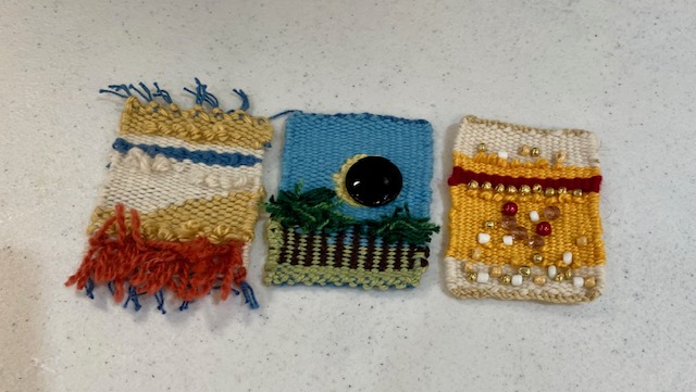 Three small abstract tapestries on a table.