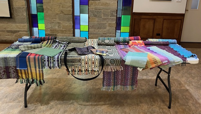 Table with a variety of handwoven fabrics and objects on it.