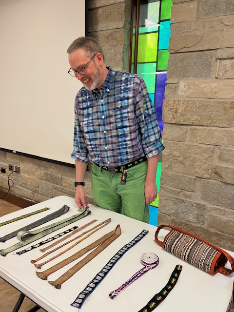 Man standing behind a table that contains several handwoven bands