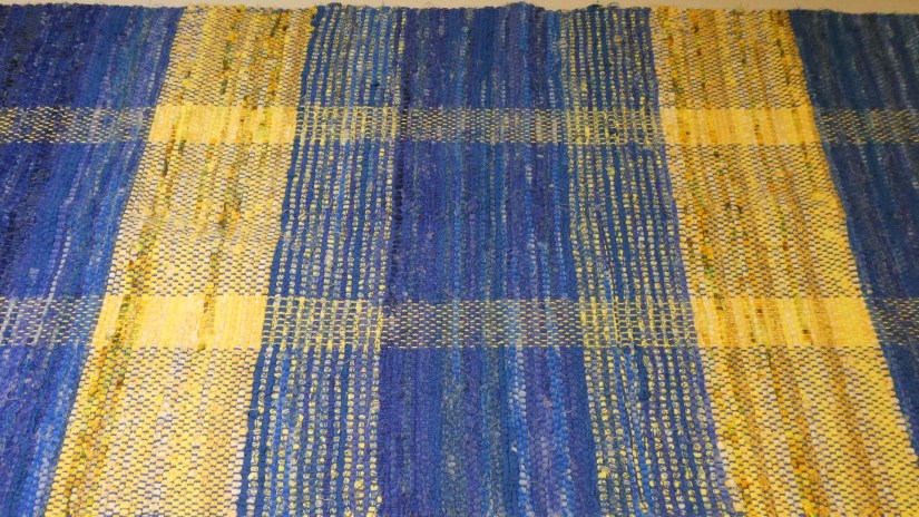 Rag rug woven with alternating solid and variegated striped of golden yellow and sapphire blue