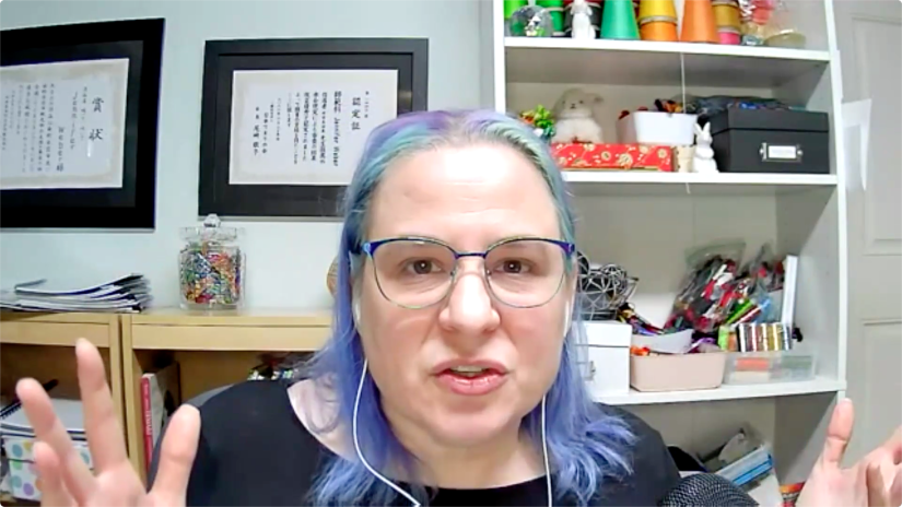 Woman wearing glasses sitting at a desk in front of a wall