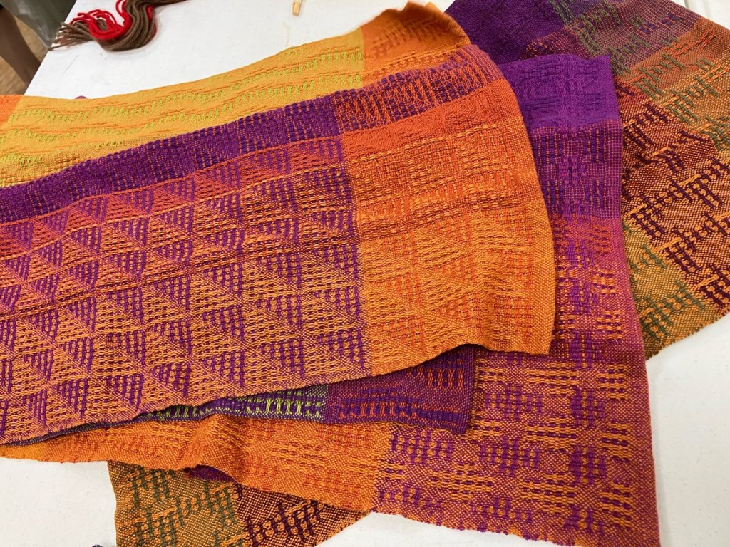 Trio of handwoven, textured towels in shades of orange, purple, yellow, and brown