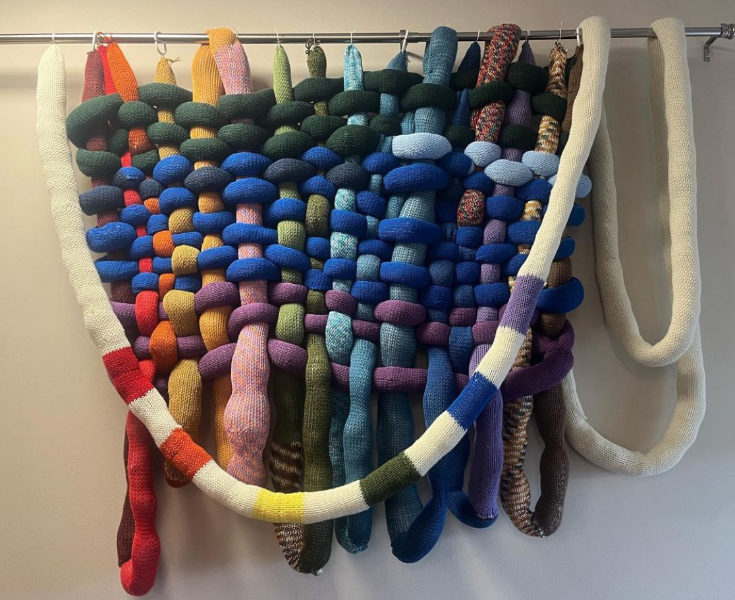 Abstract hanging made from multicolored knitted tubes arranged in a woven structure.