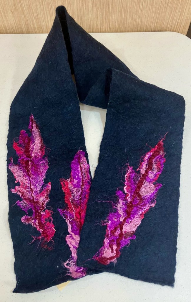 Black felted scarf with pink, purple, and red feather shapes felted on top of it.