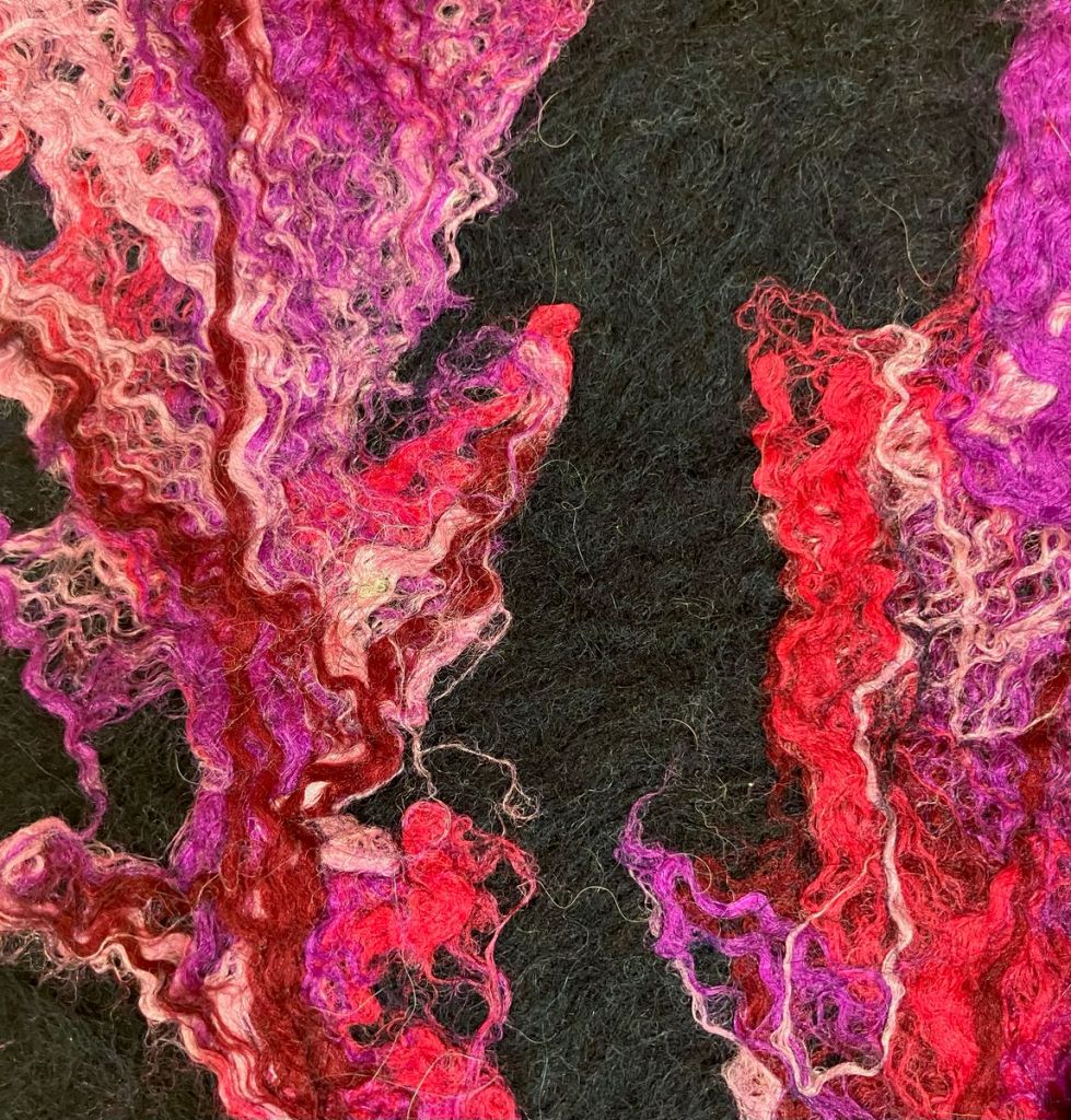 Detail, black felted scarf with pink, purple, and red feather shapes felted on top of it.