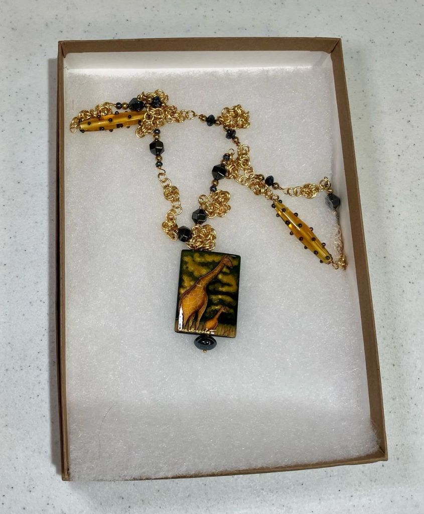 Chainmaille necklace, gold chain, black beads, long gold beads with black spots, and a focal bead showing two giraffes.