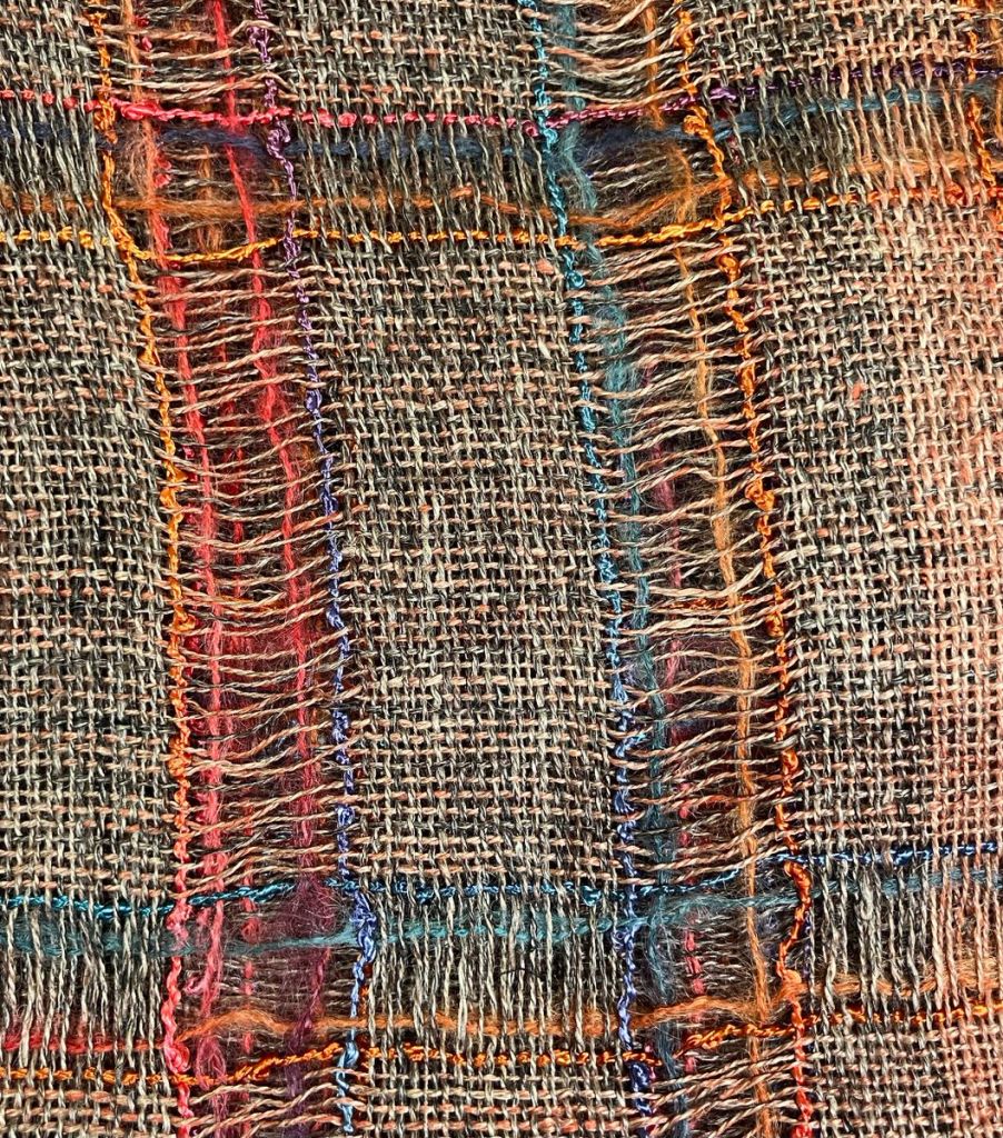 Close up of Bev. A.'s crammed and spaced shawl, brown, red, blue, and rust colors.