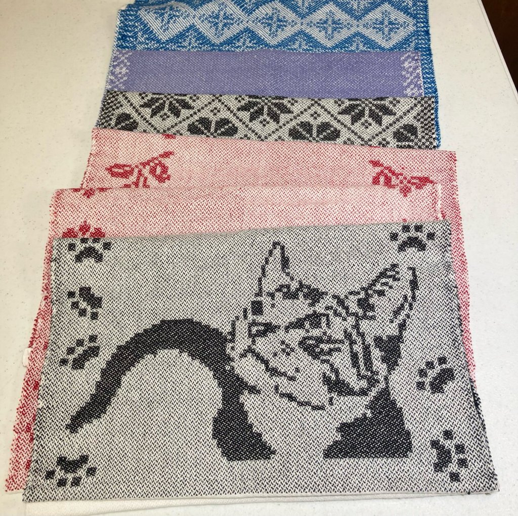 Set of towels in various colors. One with a cat picture, two with leaves, and three with geometric figures.
