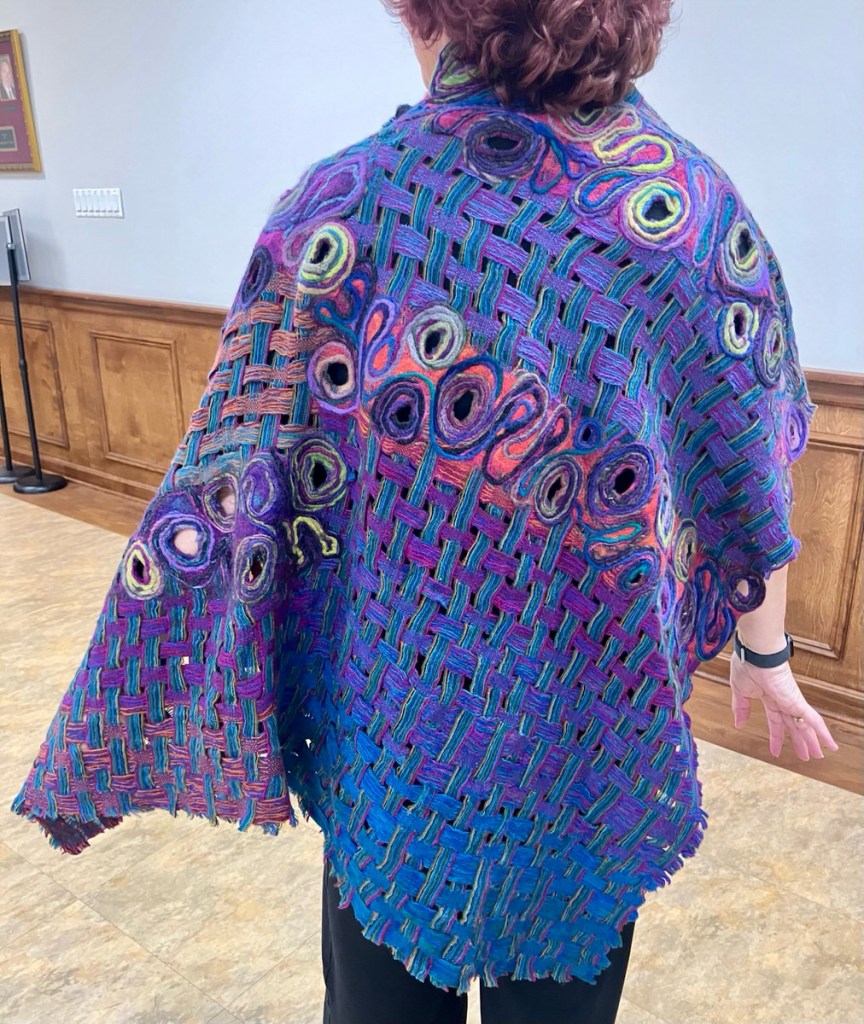 Woman wearing a felted and woven poncho in blues and purples.