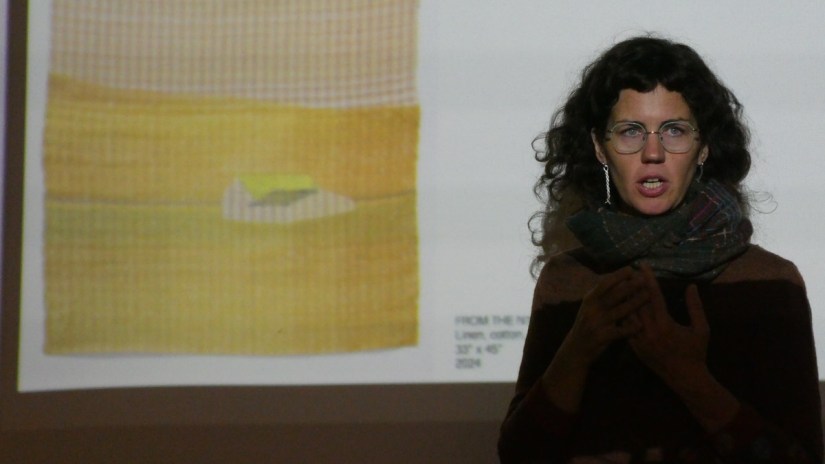 Dark-haired woman in glasses standing in front of a projected photo of a woven piece
