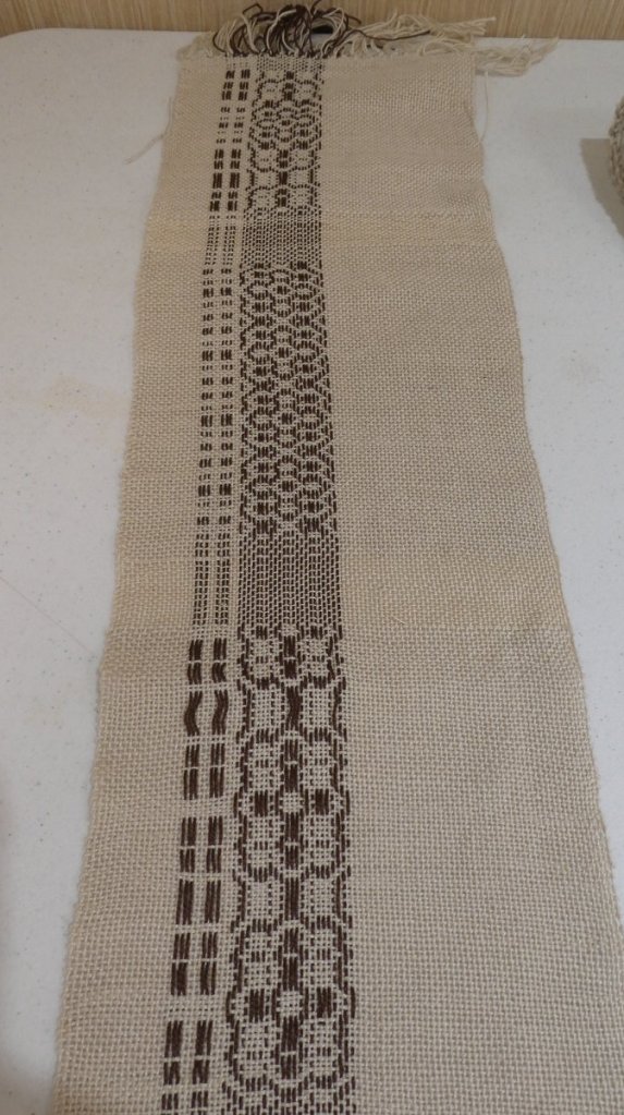 Stephanie O., sampler. Narrow strip, white background with more complex woven in black along one side.