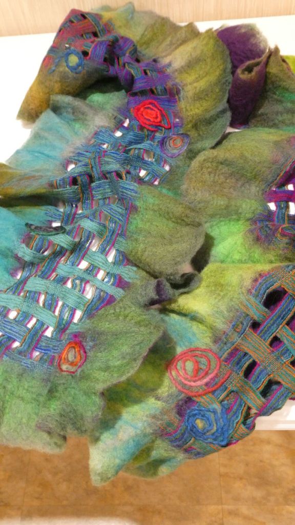 Tammy D., part of a loosely woven mostly blue and purple shawl with green felted edges and three red spiral accents.