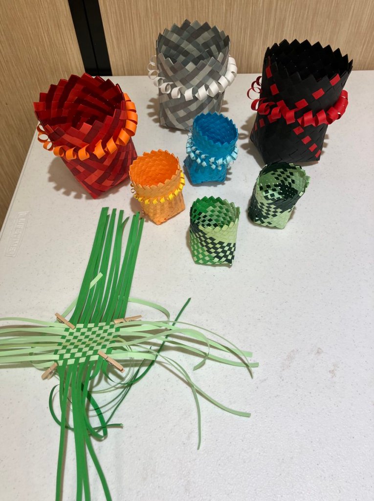 A variety of cylindrical baskets in different sizes and colors, plus one that isn't finished and shows how the base is woven.