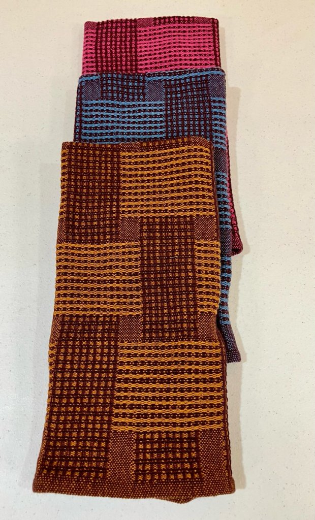 Three towels: pink and dark red, dark and medium blue, and brown and a yellowish tan.