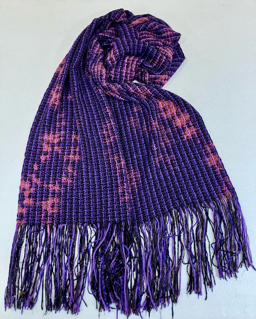 Black scarf with very thin vertical lavender stripes and fringe. There are a few patches of pinkish purple.