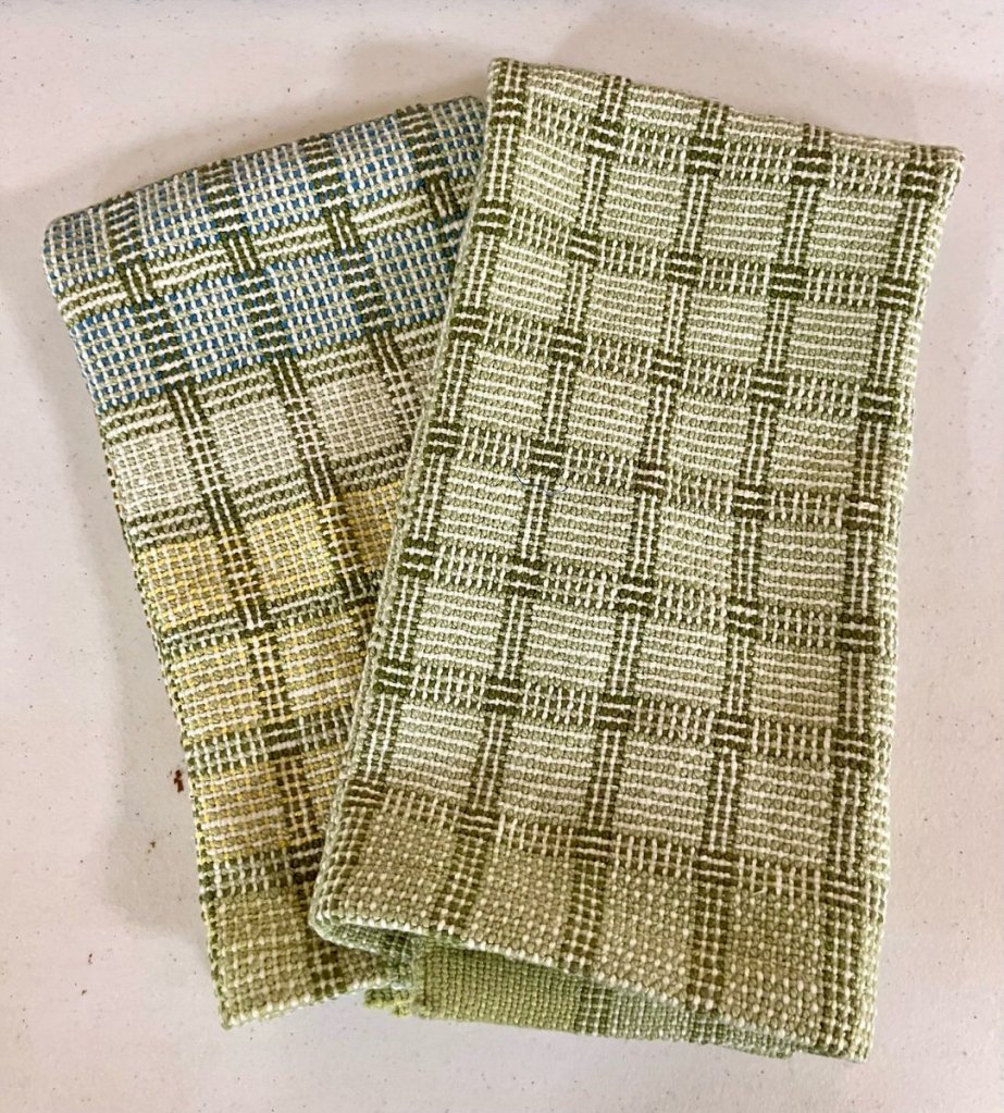 Two patterned towels woven in shades of cream, green, and blue