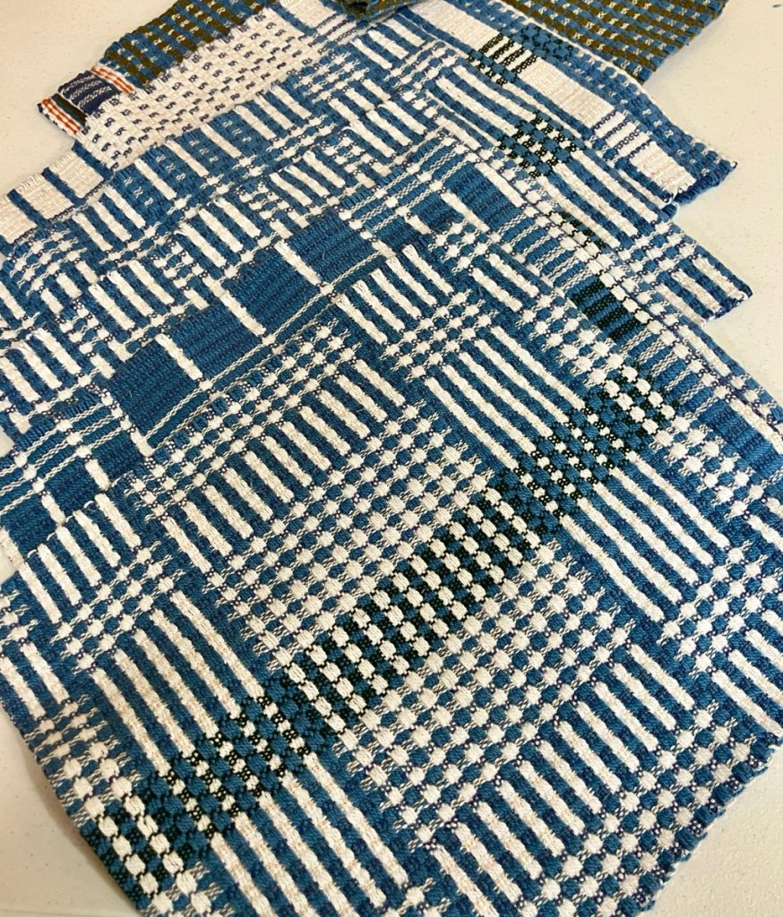 Six patterned placemats woven in shades of cream, blue, green, and in once case, red as an accent.