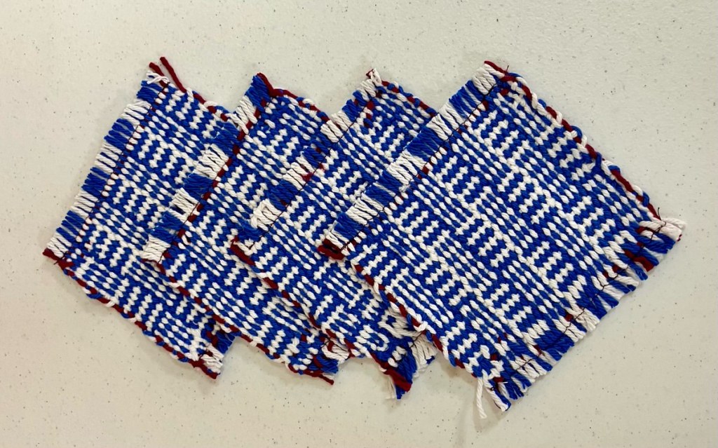 Four fringed mug rugs woven in shades of blue, white and dark red.