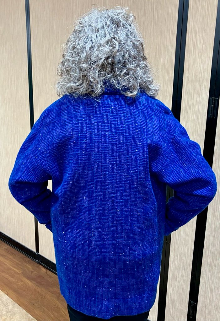 Person standing with back facing the camera, wearing a vivid blue patterned long jacket