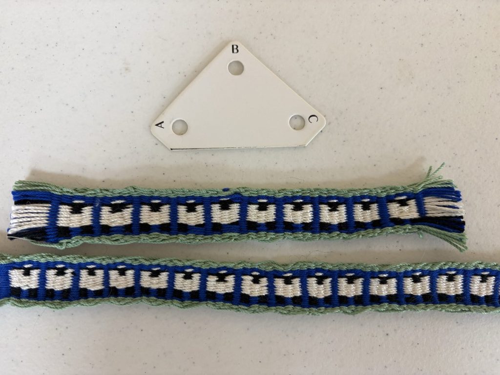 A three-sided tablet-weaving card and two tablet-woven bands with sheep motifs woven in shades of green, blue, white, and black