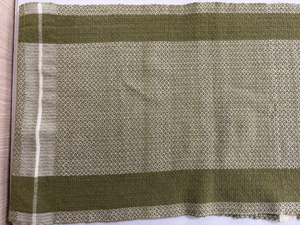 Towel woven in shades of olive green and cream in a detailed pattern with two lengthwise darker green wide stripes near the edges