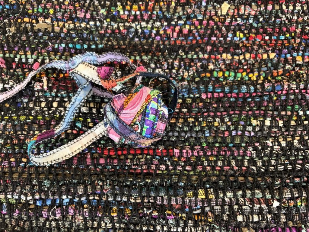 Close-up view of rug woven in black and bright colors, with a ball of the bright-colored weft ribbon yarn created from fabric scraps