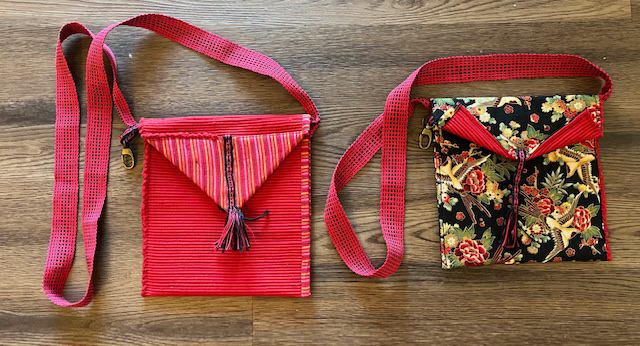 Two bags, red on one side, black fabric with flowers and birds on the other. Both have long red woven straps and fringed tabs.