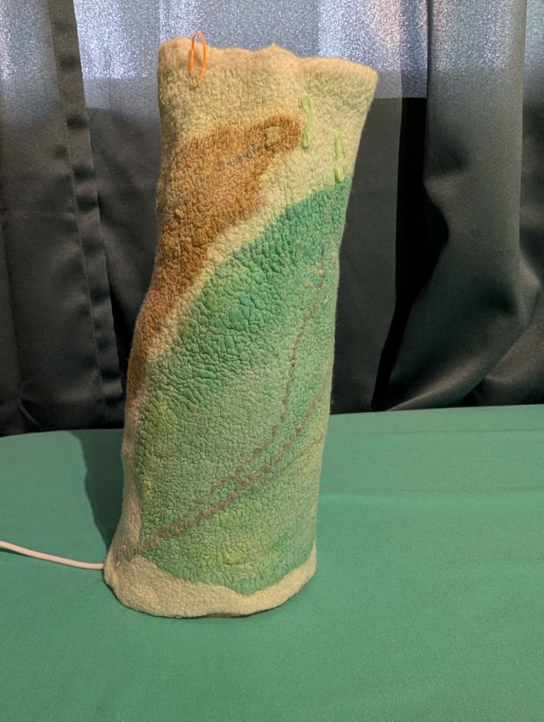 Luminary 2. Unlit. Off-white tall columnar luminary with a green leaf design.