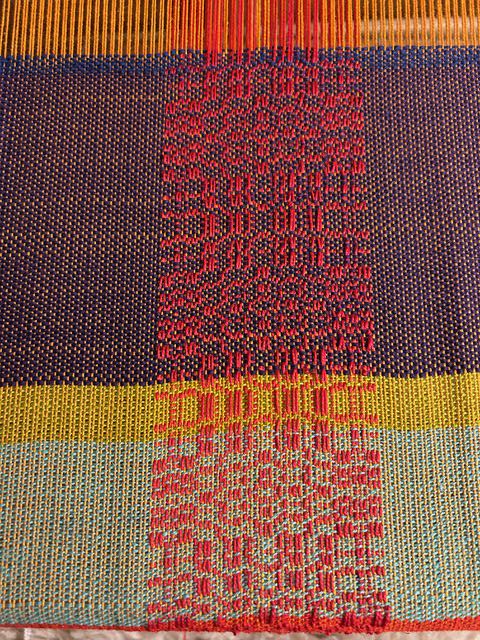 Thin section of overshot using a red weft on a plain woven piece done with wefts in multiple colors.