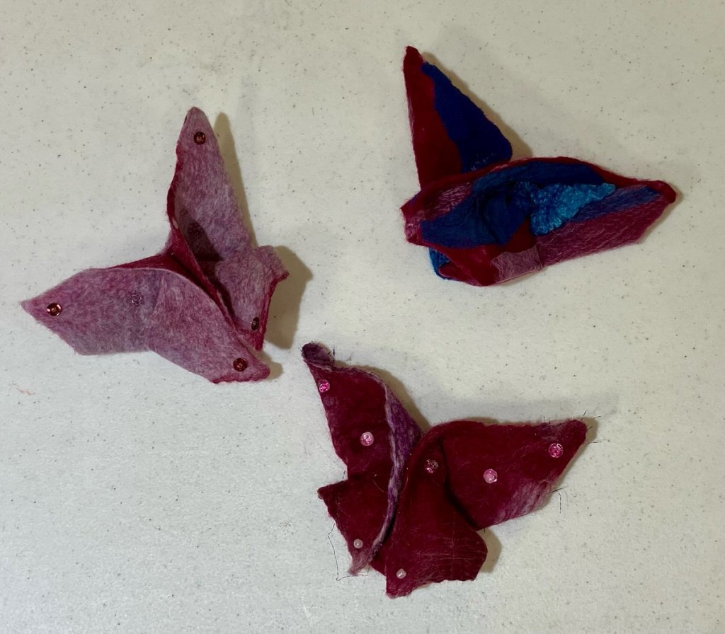 Three felt butterflies in various shaded of blue, dark red, and pink with some embellishments.