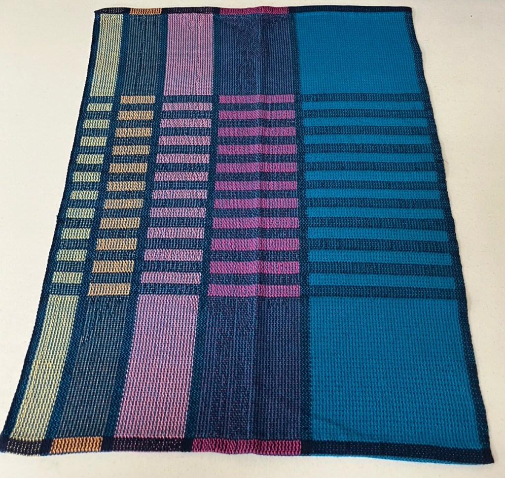 A breadcloth using five vertical stripes of different colors with some thin horizontal strips using only one color of warp in the center.