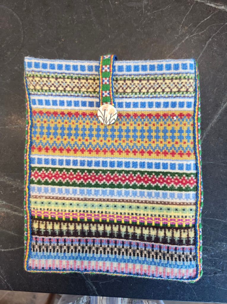 Multi-colored krokbragd notebook/iPad case with a Sami band and button to close it.