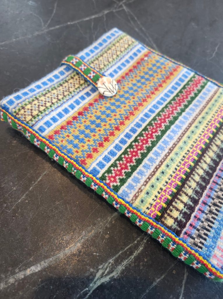 Multi-colored krokbragd notebook/iPad case with a Sami band and button to close it.